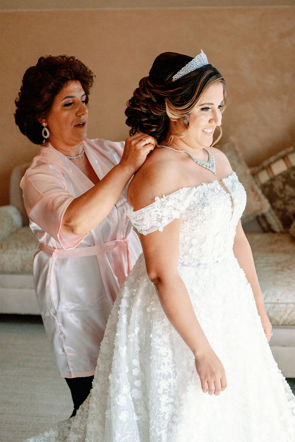 A bride is helped with her diamond necklace while getting ready with mom