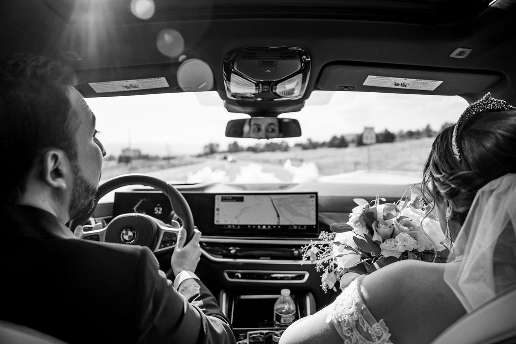 Black and white image looking over the shoulder of newlyweds in a BMW