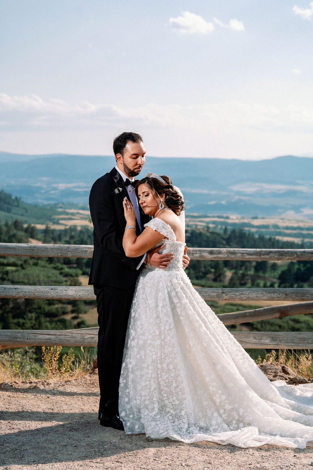 Newlyweds snuggle on a mountain overlook by a rustic wood fence