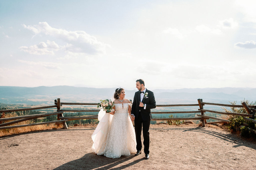 A bride and groom walk away from an epic overlook holding hands at Cielo At Castle Pines
