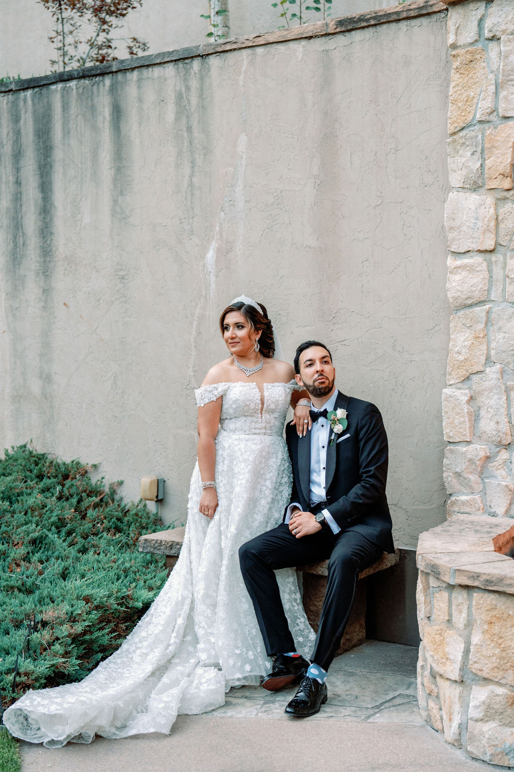 A bride lans on her groom's shoulder as he sits on a garden bench at Cielo At Castle Pines
