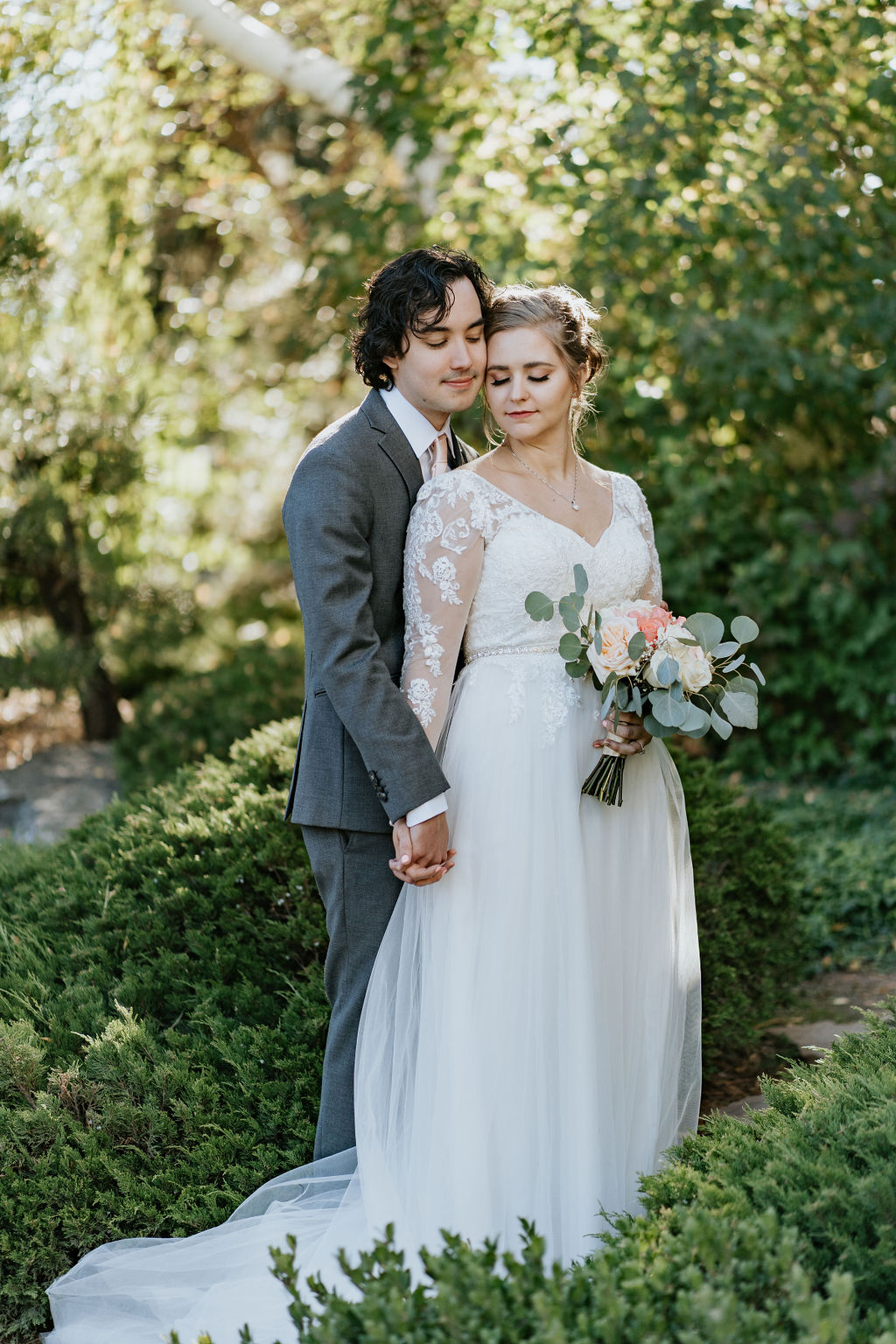Newlyweds snuggle in a lush garden at sunset while touching cheeks at one of the Boulder wedding venues
