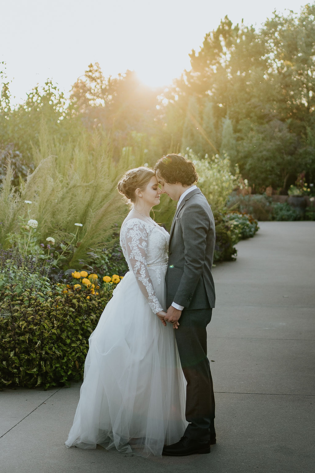 A bride and groom hold hands while touching foreheads in the gardens at one of the Boulder wedding venues at sunset