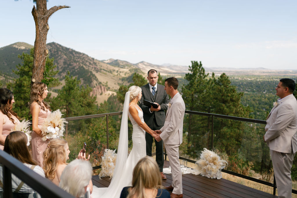 Newlyweds hold hands on a porch deck during their ceremony at one of the Boulder wedding venues