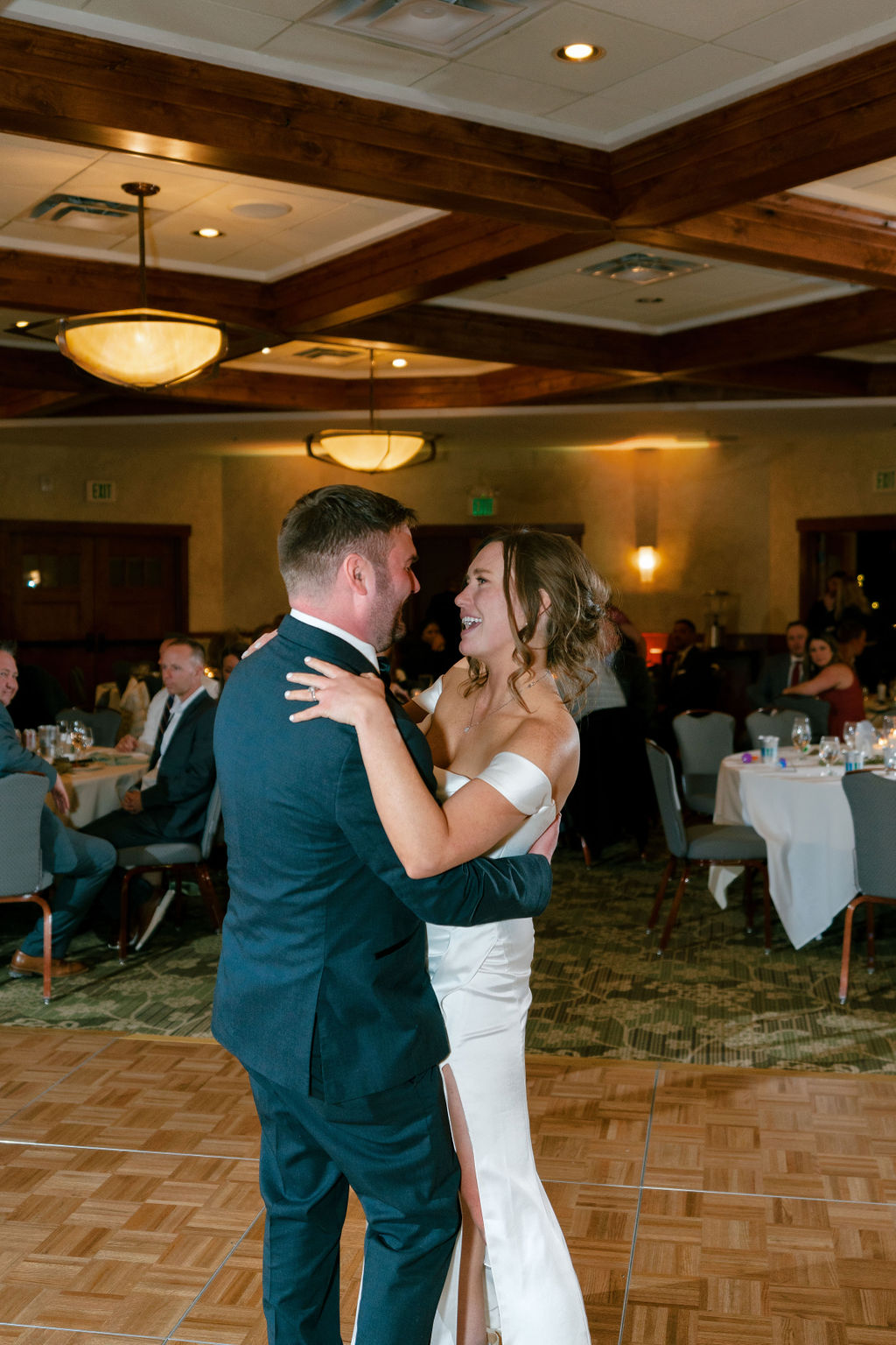 A bride and groom dance on the dance floor for the first time as guests sit looking on