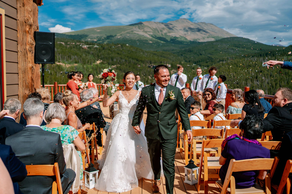 Newlyweds hold hands walking up the aisle to end their mountain ceremony as guests throw confetti