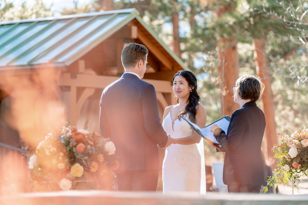 A bride and groom hold hands during their sunset ceremony while listening to the officiant