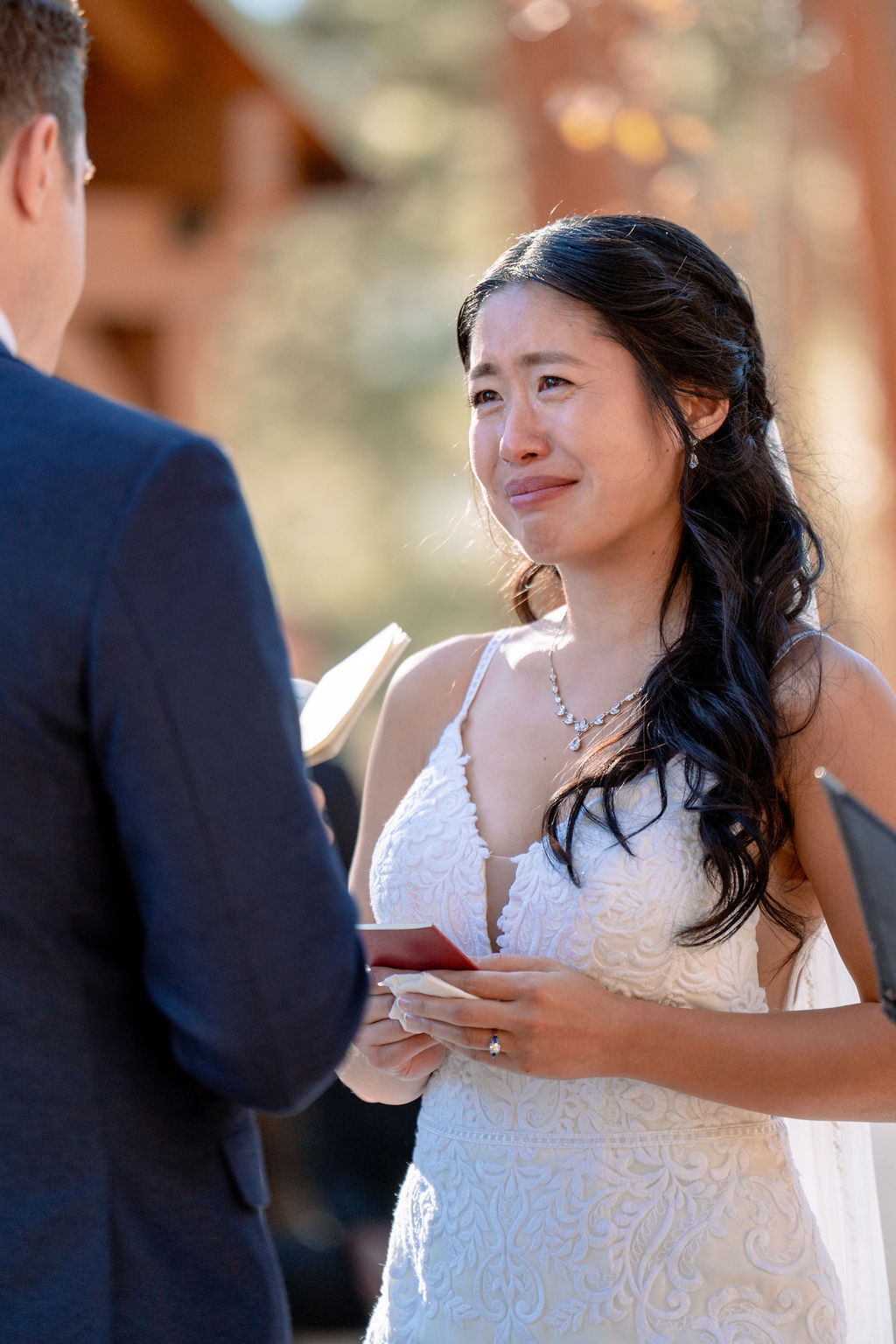 A bride cries while listening to her groom read from a notebook during their ceremony