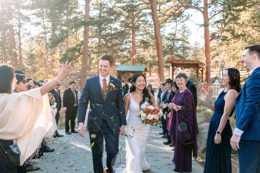 Guests throw leaves as newlyweds walk up a sidewalk smiling big at their Della Terra Wedding