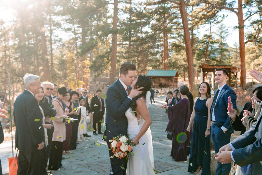 Newlyweds kiss while surrounded by guests on a stone path