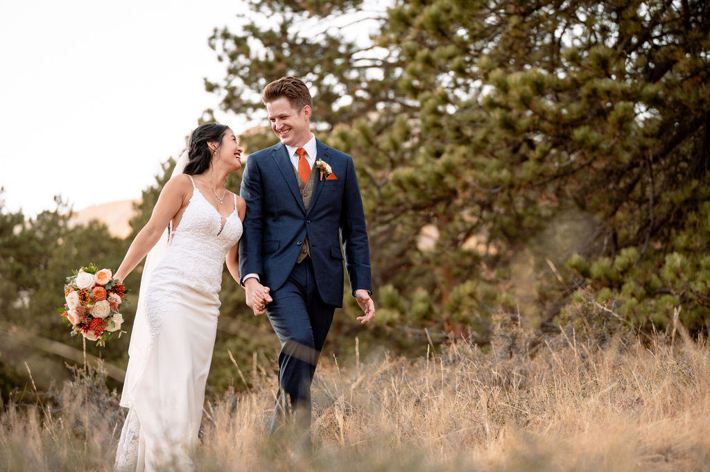 A bride and groom laugh and hold hands while hiking during their Della Terra Wedding