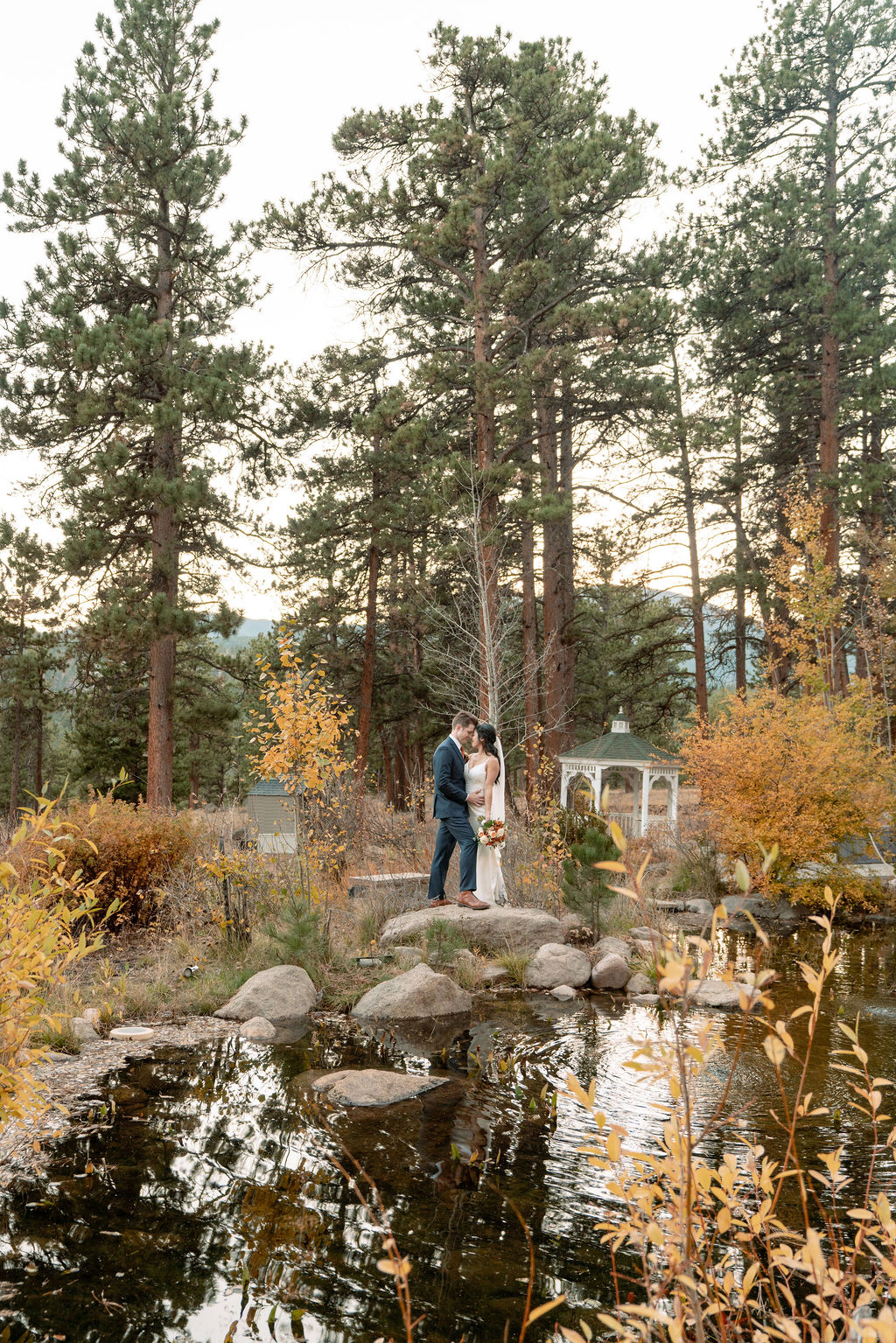 Newlyweds touch foreheads while hugging on a rock on a pond at their Della Terra Wedding