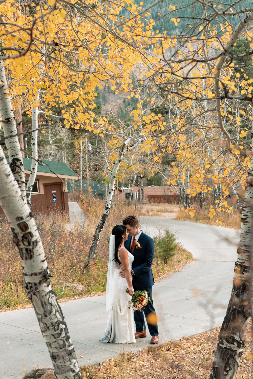 A bride and groom snuggle in the aspens on a sidewalk touching foreheads at the Della Terra Wedding venue
