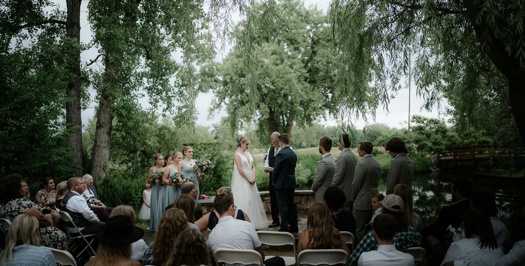 Newlyweds stand at the altar under a willow tree at their hudson gardens wedding ceremony listening to the officiant