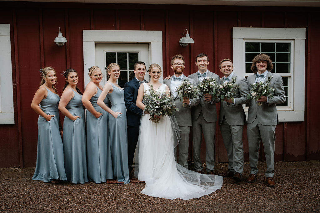 Newlyweds stand with their wedding party outside a red building