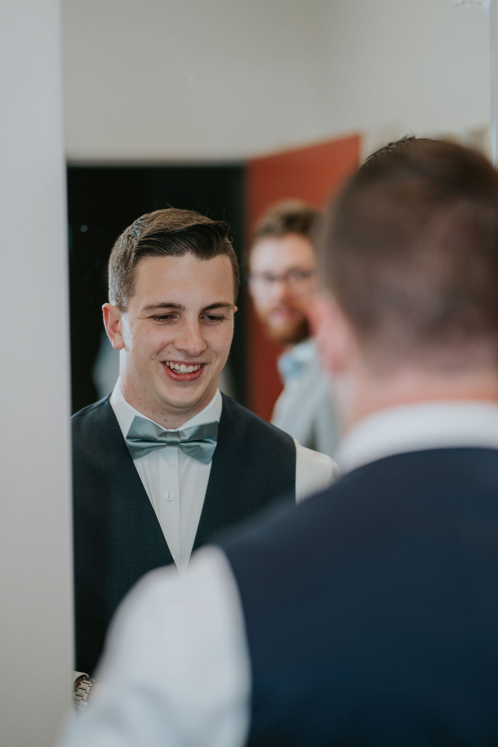 A groom smiles in a mirror while getting ready