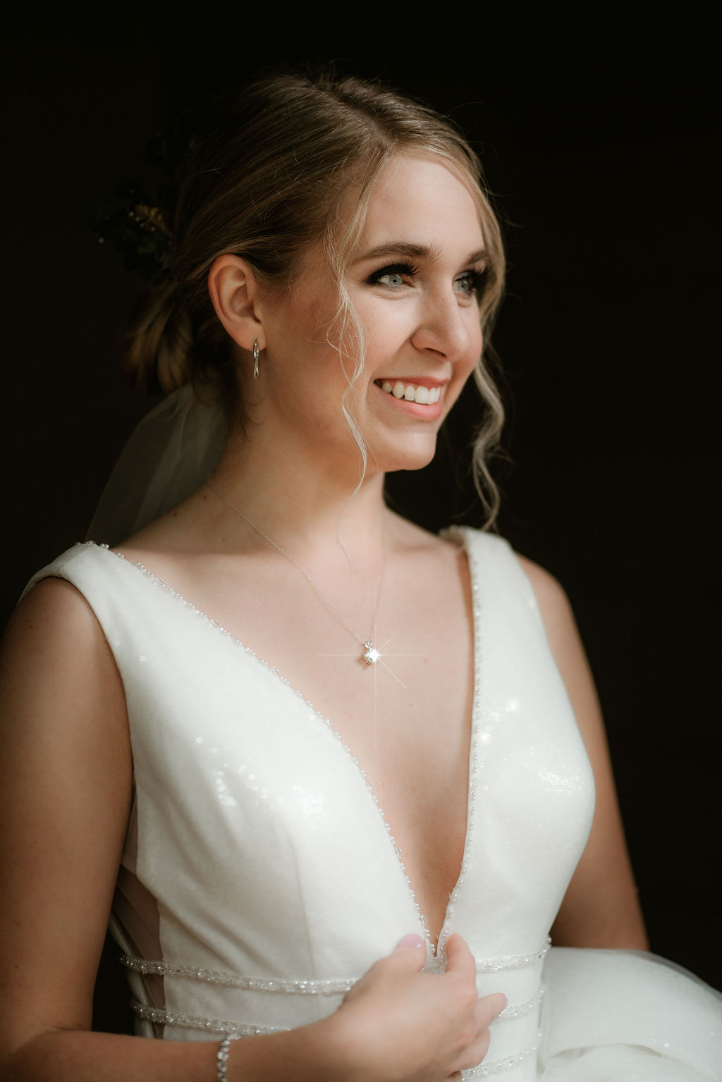 A bride smiles big in her gown as her diamond necklace glistens