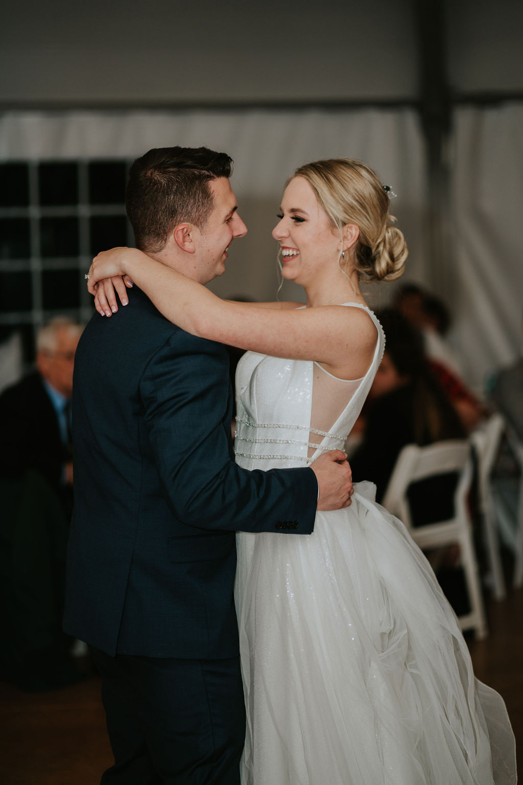 Newlyweds share their first dance with big smiles under a tent