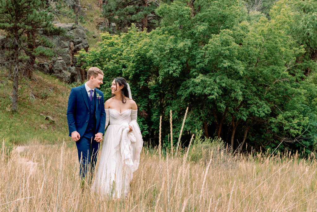 Newlyweds smile and walk hand in hand through tall golden grass