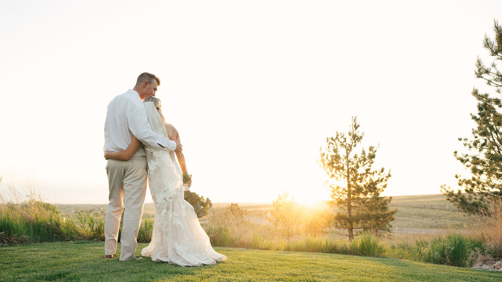 Newlyweds cuddle while watching the sunset from a hilltop