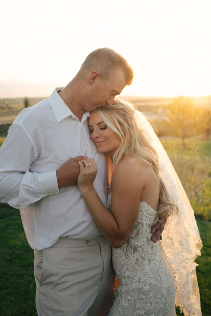 A bride snuggles into the chest of her groom as they admire the sunset