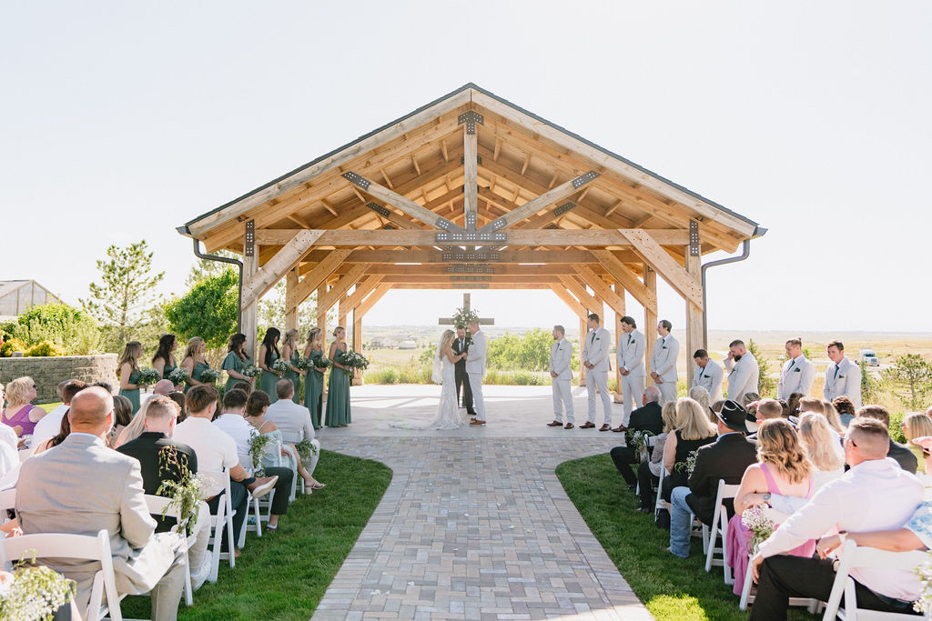 A bride and groom hold hands at the altar under a gazebo in front of a cross at one of the wedding venues near Denver