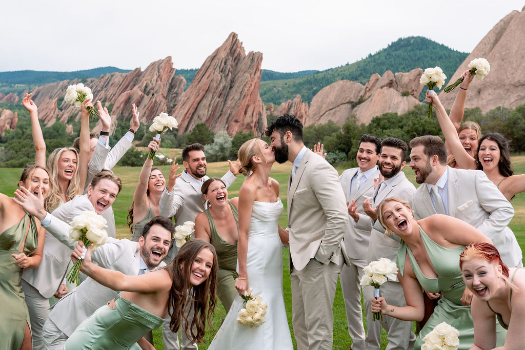 A bride and groom kiss as their wedding party goes wild around them holding white roses