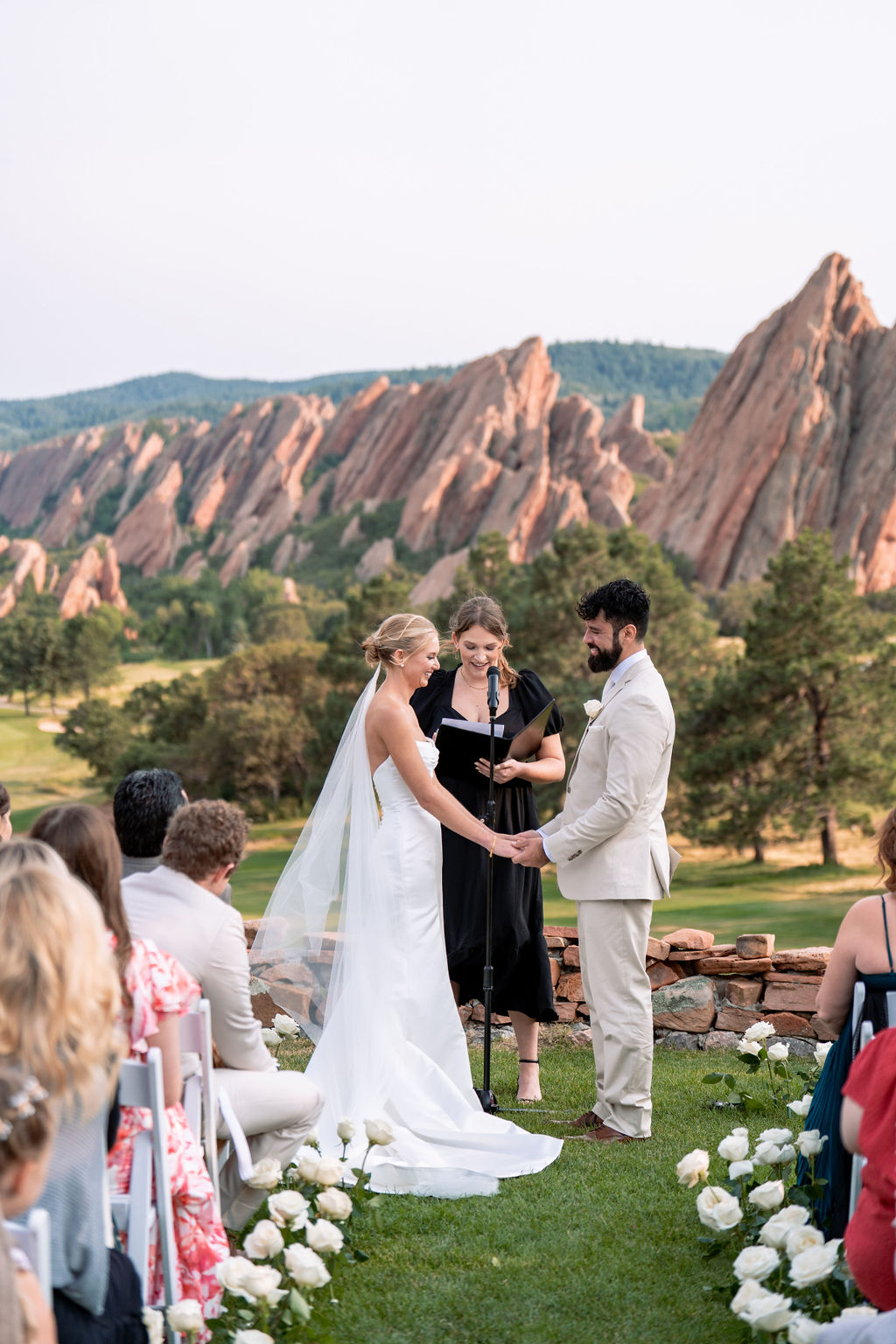 Newlyweds hold hands while smiling during their outdoor ceremony at one of the wedding venues near Denver