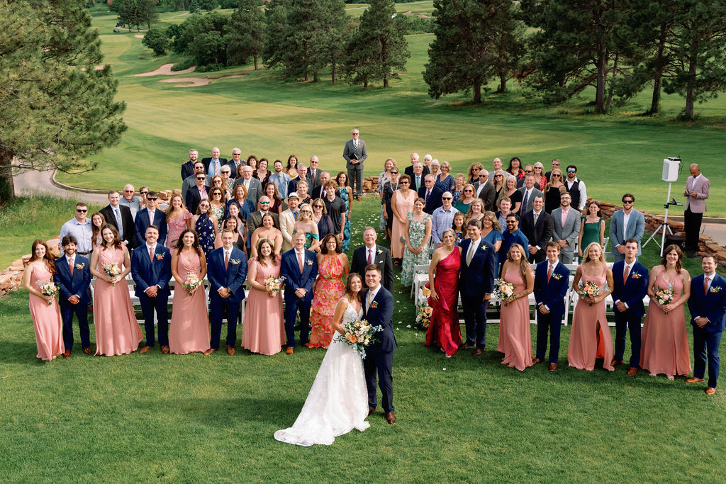 A look down to a wedding taking place in the lawn of a golf course with everyone standing and smiling