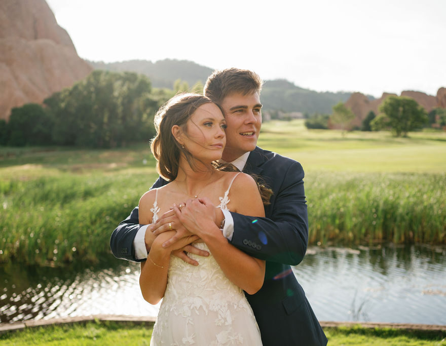 A bride and groom hug while standing by a pond at one of the stunning outdoor wedding venues near Denver