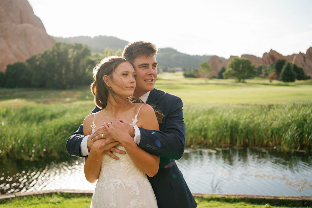 A bride and groom hug while standing by a pond at one of the stunning outdoor wedding venues near Denver