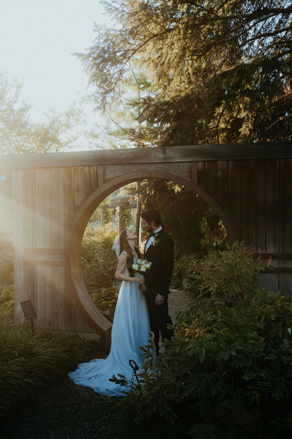 A bride and groom smile at each other under a wooden circle arch at sunset at one of the wedding venues near Denver
