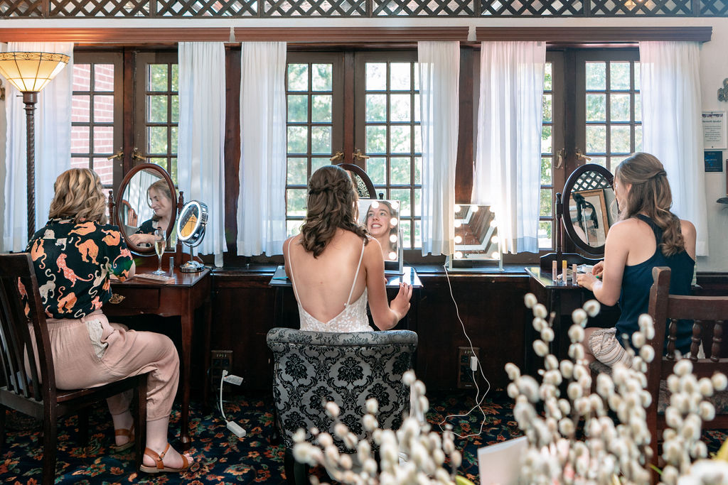 A bride siles while getting ready in a lighted mirror