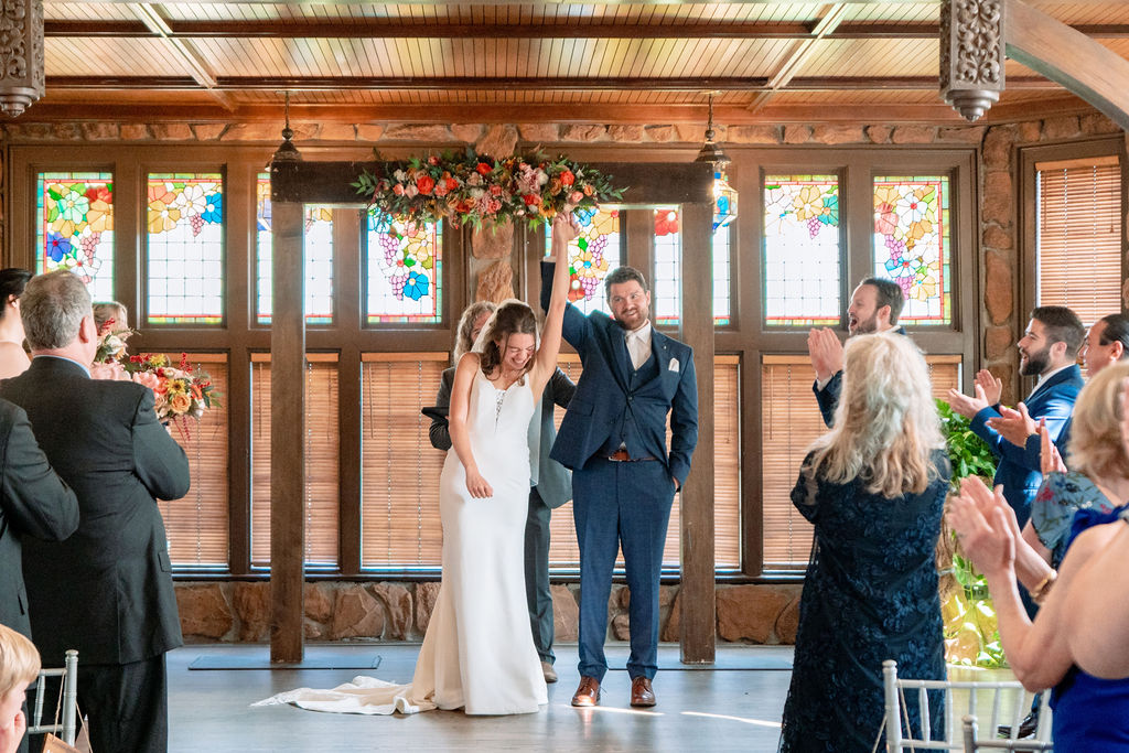 Newlyweds raise their hands and celebrate to tend their ceremony as guests clap