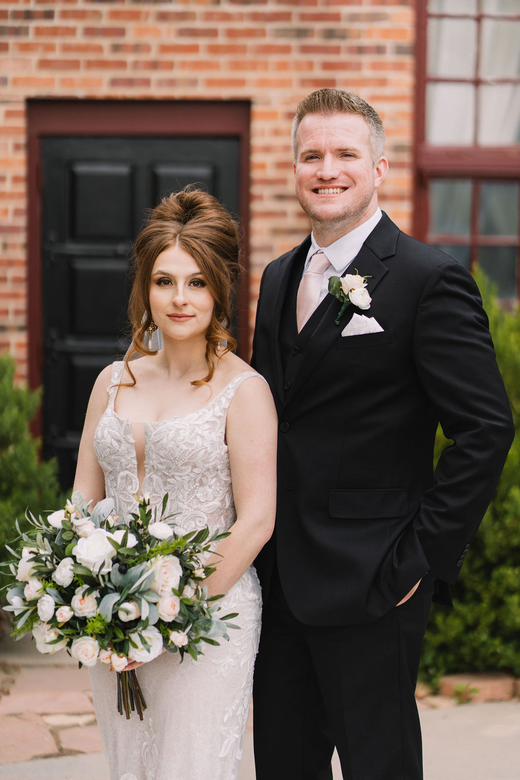 A bride and groom stand together on the wellshire event center wedding venue patio with hands in pockets and holding the white bouquet