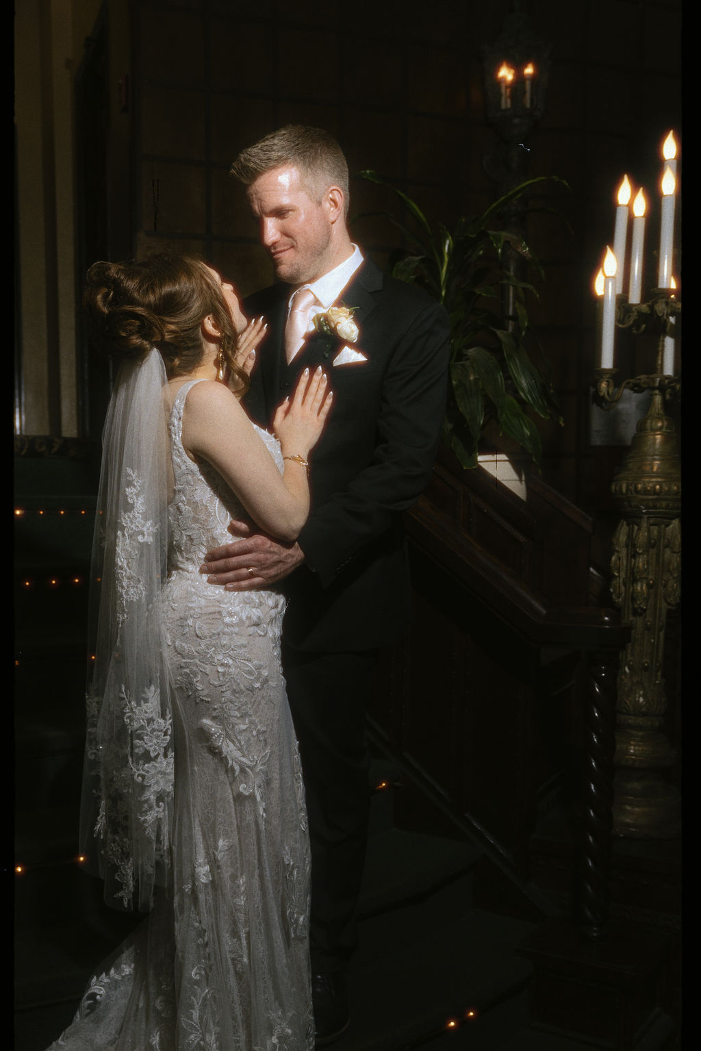 Newlyweds cuddle by candles while smile at each other in a dark room